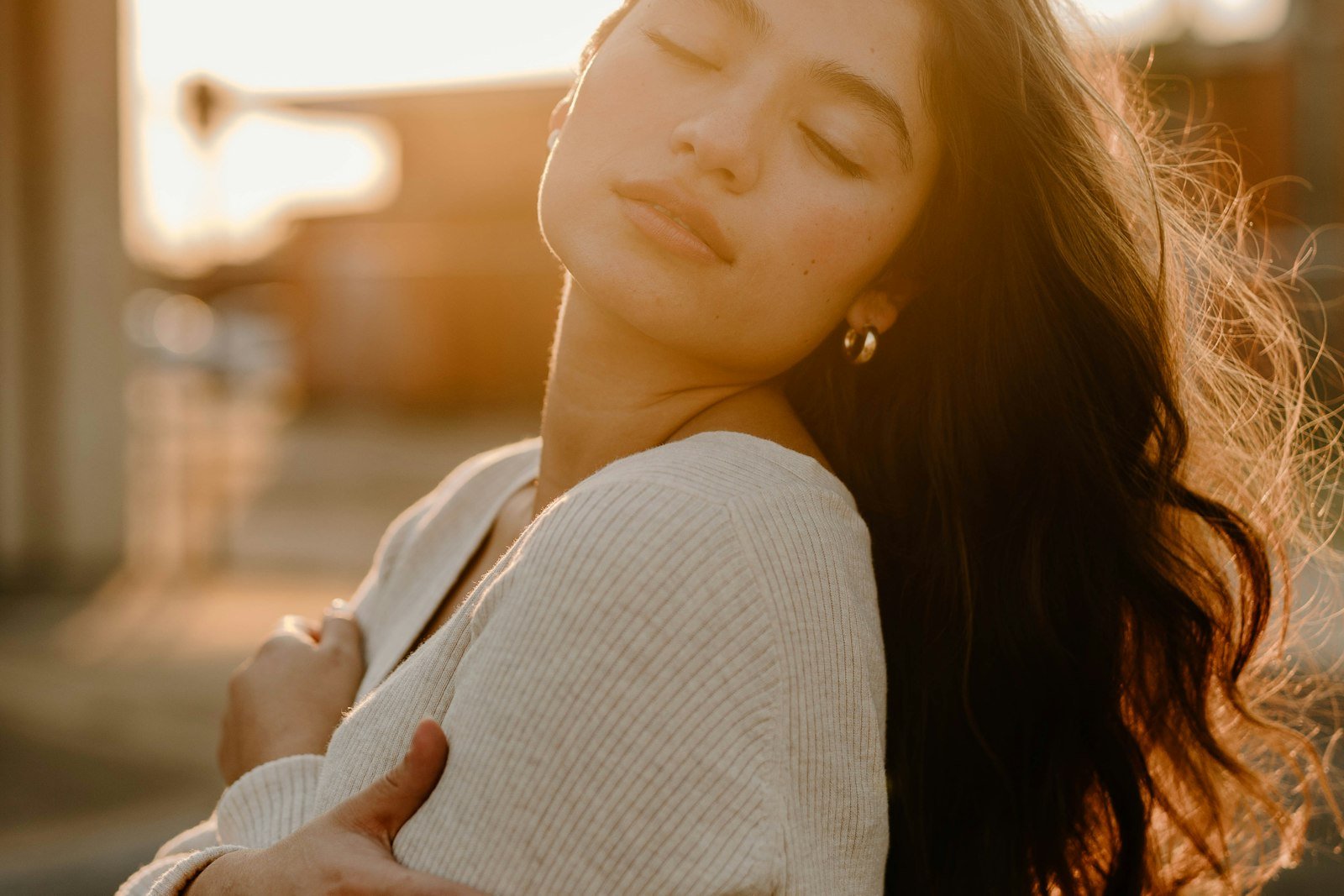 Mulher de olhos fechados abraçando a si mesma, sob a luz quente do fim de tarde