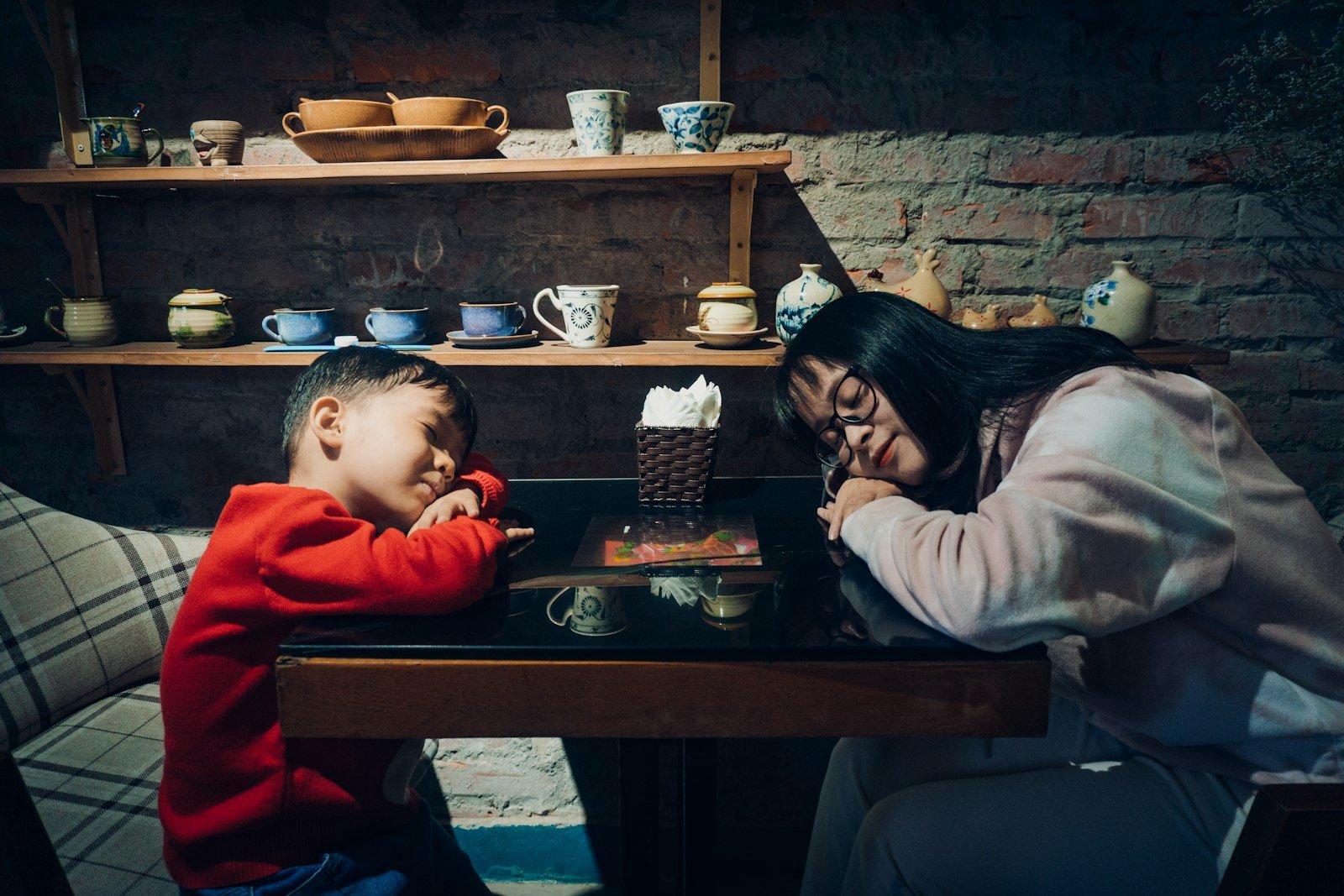 Mãe e filho cansados, com a cabeça apoiada na mesa da sala